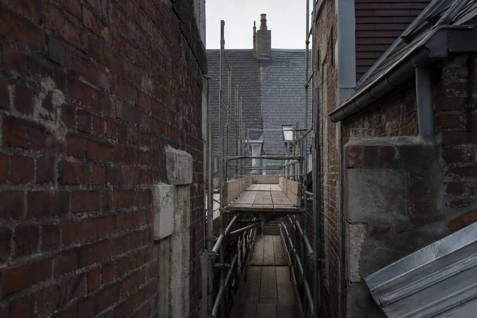 Échafaudage monté dans une rue étroite de courée, entre deux façades de brique très rapprochées