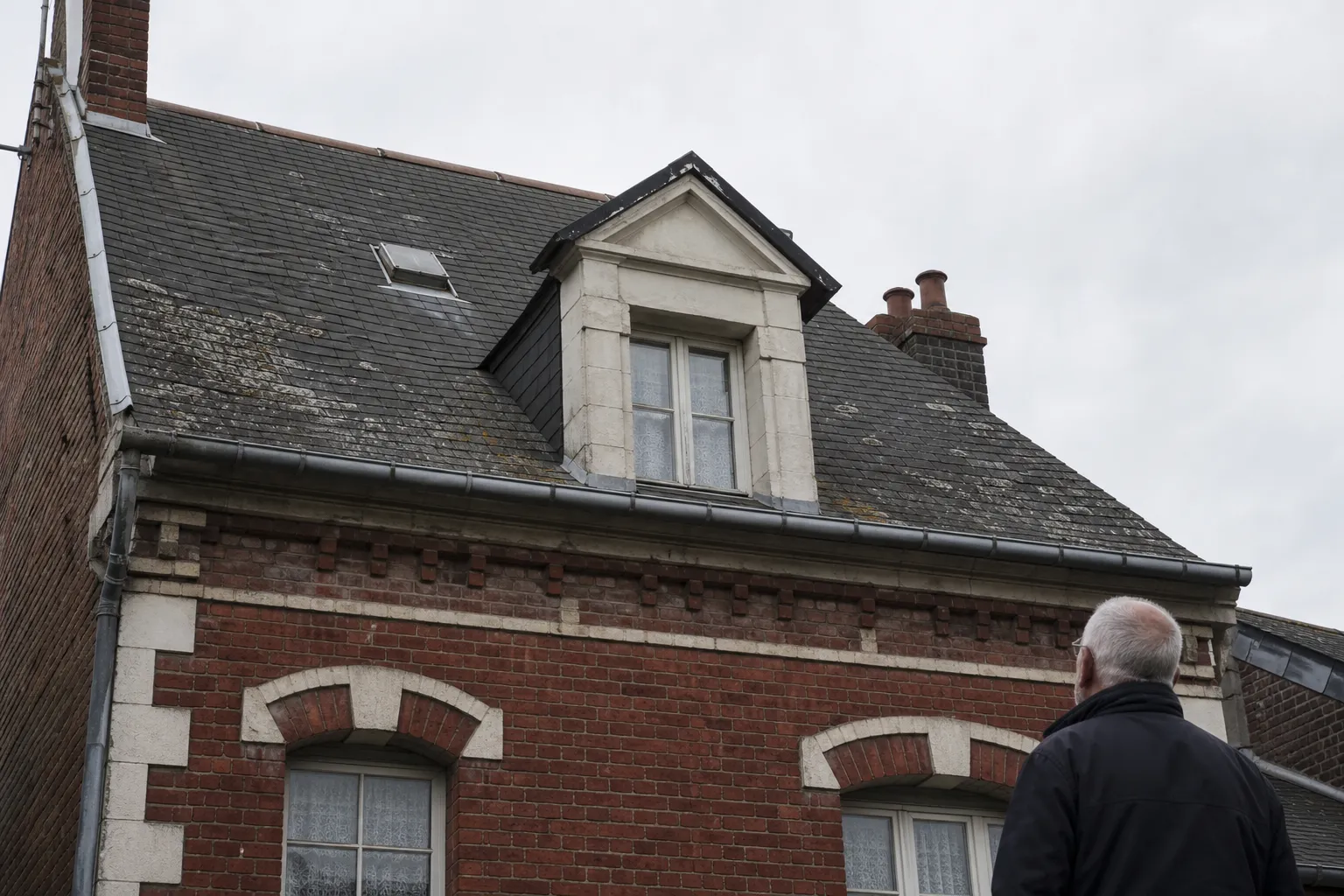 Maison de brique des années 1930 vue depuis la rue, toiture à forte pente et lucarne centrale