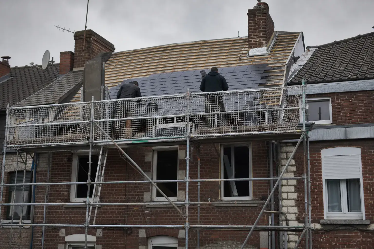Chantier de couverture sur une maison de ville en brique rouge, échafaudage monté en pignon et bâche de protection